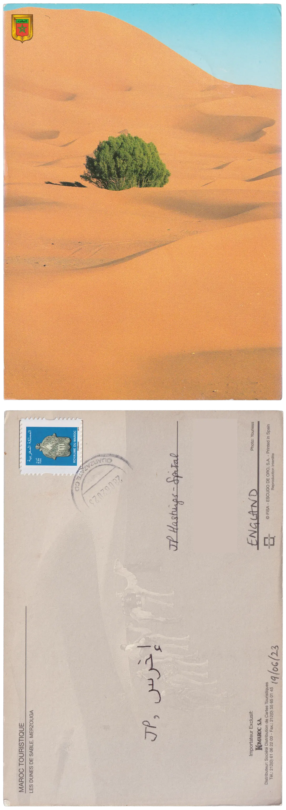 Both sides of a postcard. On the front: The undulating dunes of a desert, with a single green bush in the middle, and a small corner of blue sky. On the back: JP, إخرس